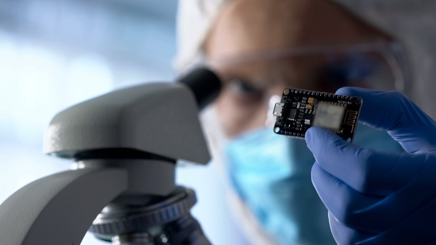 Technician examining a circuit board under a microscope in a controlled environment